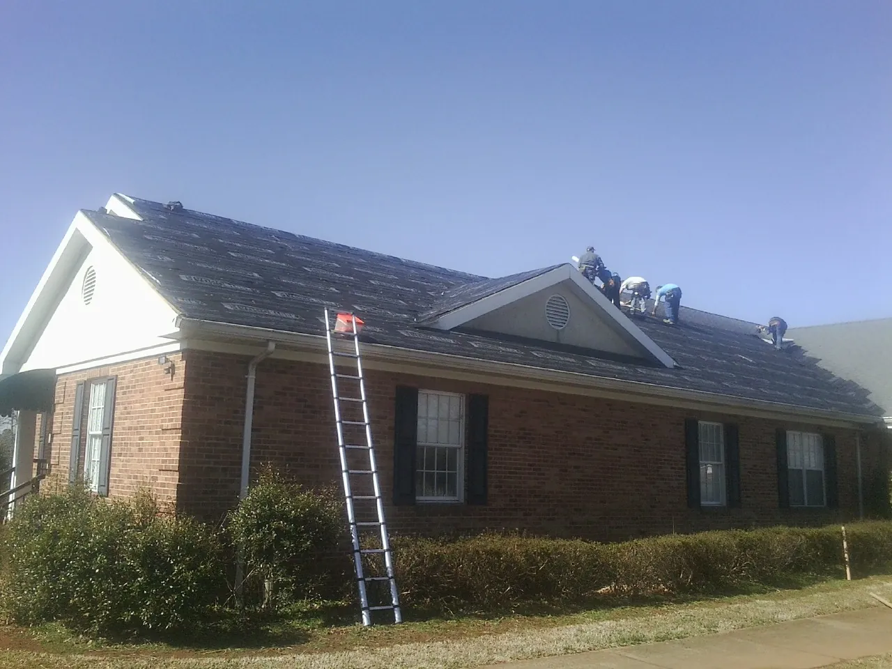 Crew tearing shingles off a brick ranch roof with a ladder set — Metal Roof Repair work by our crew in Dundee